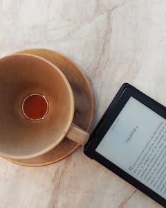 Top view of an e-reader and empty coffee cup on a marble table.